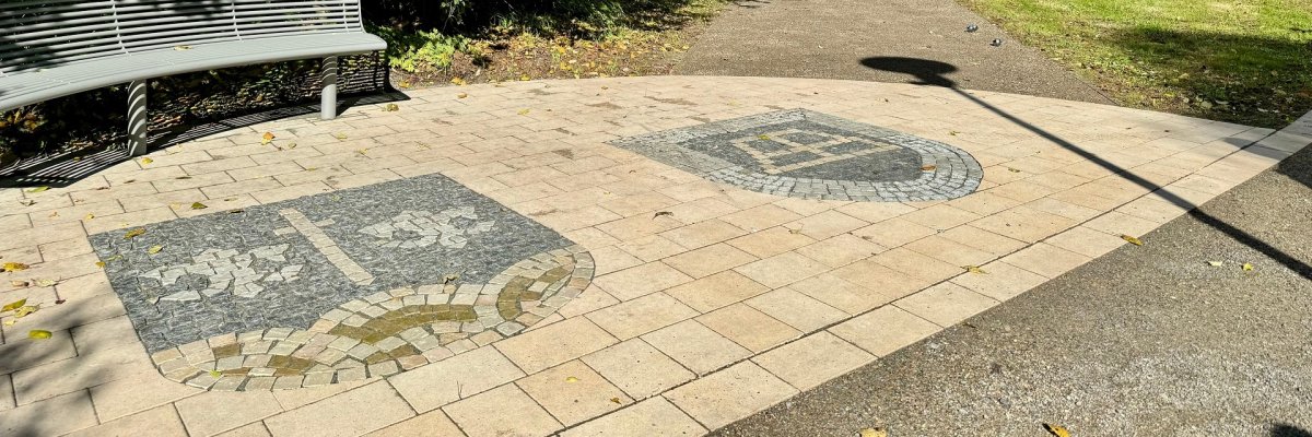 Kurpark-Eröffnung 3 Eine Boulebahn, auf der gerade zwei Männer eine Partie spielen. Im Vordergrund ist ein kleiner gepflasterter Platz auf dem das Wappen der Gemeinde und das Wappen von Stemwedes Partnerstadt Lardy eingepflastert wurden.