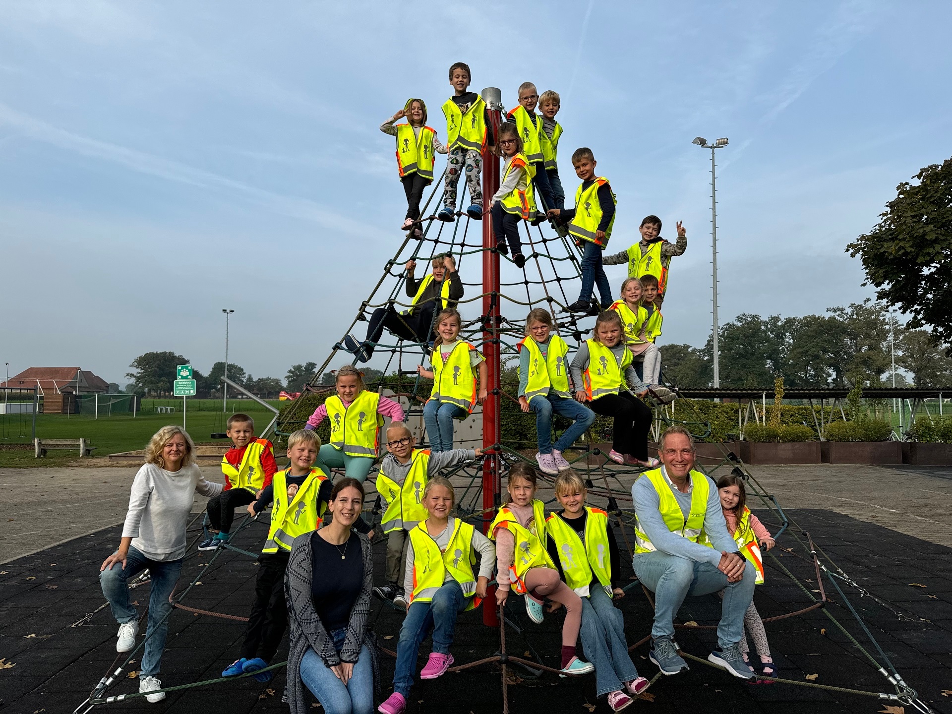 Die Erstklässlerinnen und Erstklässler der Grundschule Oppenwehe haben sich auf einem Klettergerüst verteilt. Sie alle trage die gelben Warnwesten. Auf dem Bild sind auch zwei Klassenlehrerinnen und ein Mitarbeiter der Gemeinde Stemwede zu sehen. 