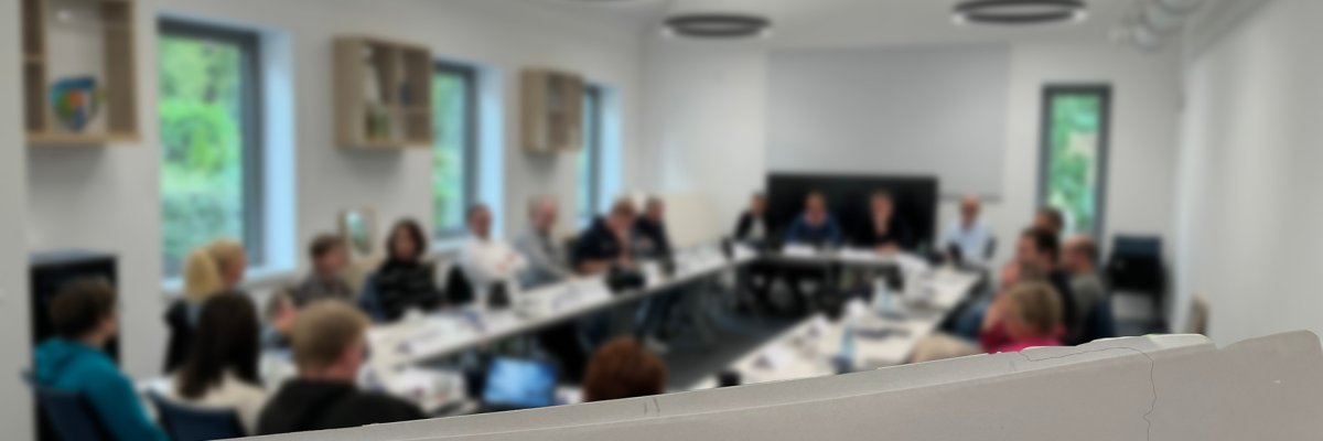 Sicherheitskonferenz 2024 Ein nur unscharf zu erkennender Sitzungssaal in dem zahlreiche Personen sitzen. Im Vordergrund ist ein Papier zu sehen auf dem folgendes steht: Stemweder Sicherheits- und Integrationskonferenz, September 2024".