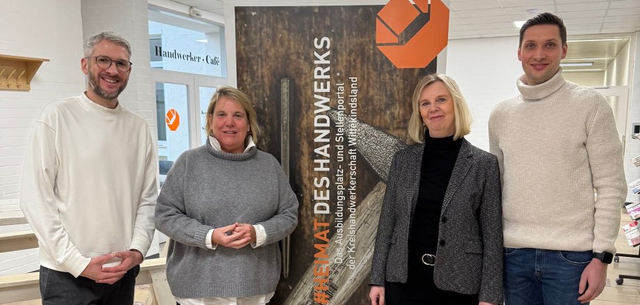 Zwei Männer und zwei Frauen stehen an einem Infobanner der Kreishandwerkerschaft Wittekindsland, auf dem steht "Heimat des Handwerks".
