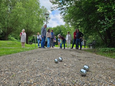 Mehrere Menschen, die in einem Park Boule spielen.