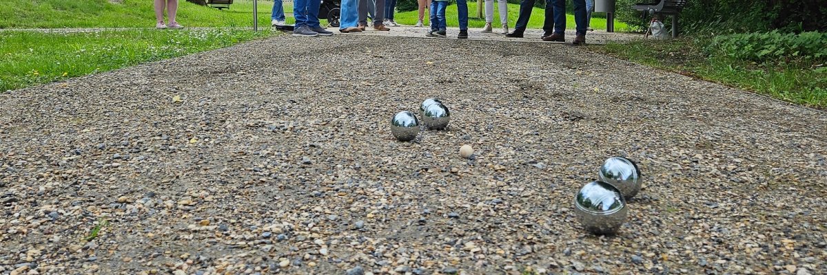 Mehrere Menschen, die in einem Park Boule spielen.
