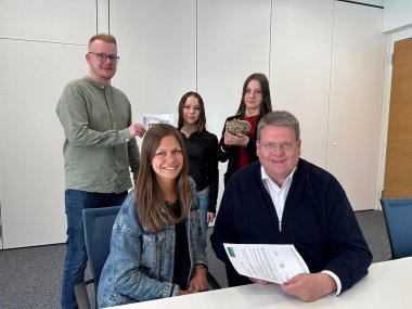 Gruppenfoto mit insgesamt 5 Personen. Im Vordergrund sitzen eine junge Frau und rechts daneben ein Mann. Dahinter stehen zwei junge Damen und ein junger Mann, die alle in die Kamera lächeln. Die Personen im Vordergrund halten einen bemalten Stein in den Händen.