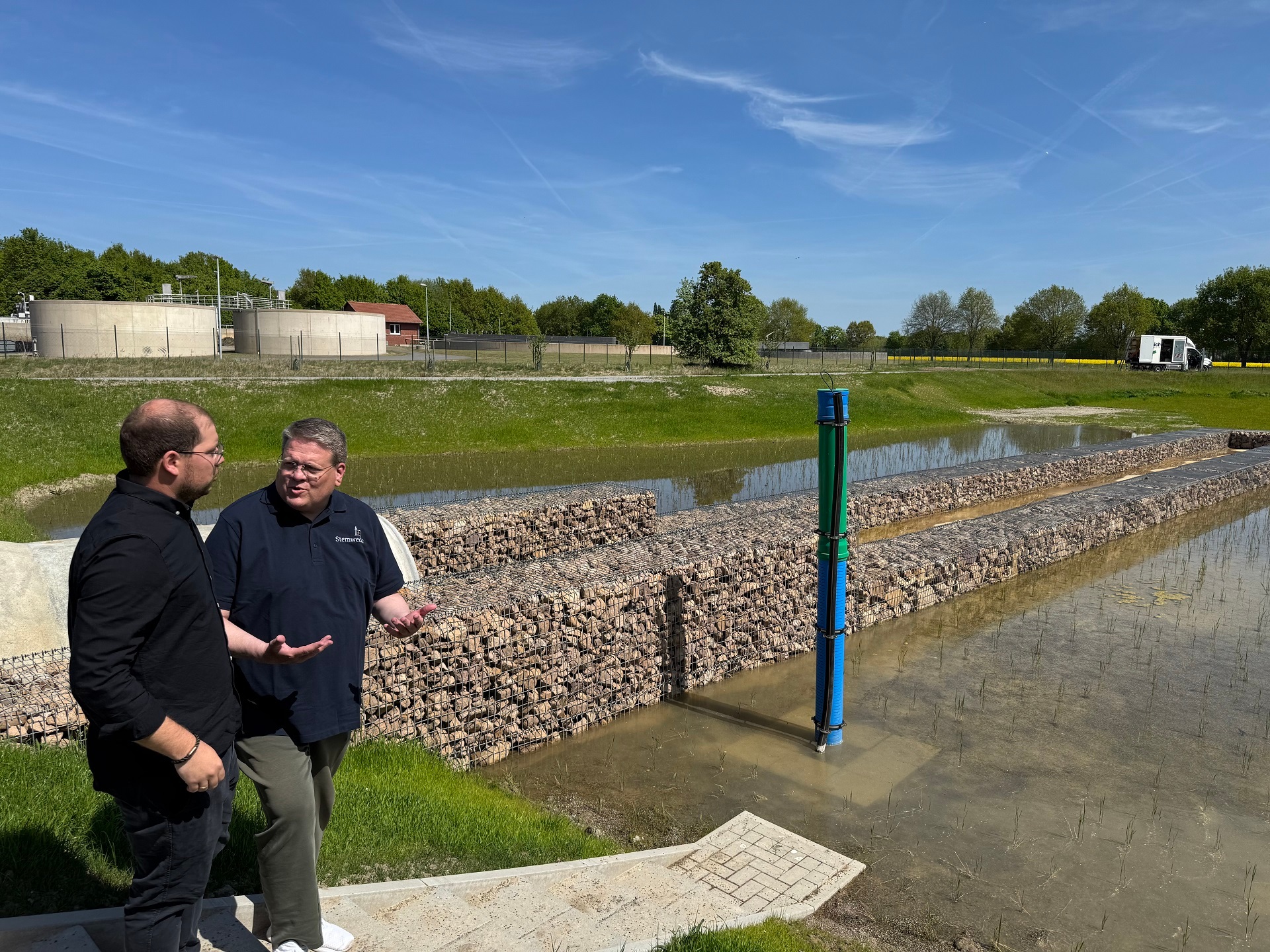 Zwei Männer stehen an einem künstlich angelegten Teich der als Filter an einer Kläranlage dient.