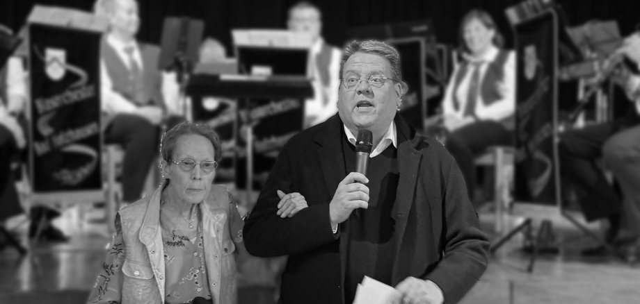 Doris Schwier Eine schwarz-weiß-Aufnahme zweier Personen, die gerade scheinbar ein Publikum begrüßen. Im Hintergrund ist verschwommen eine Blaskapelle zu erkennen. Da es eine schwarz-weiß-Aufnahme ist, scheint es sich um einen Nachruf zu handeln.