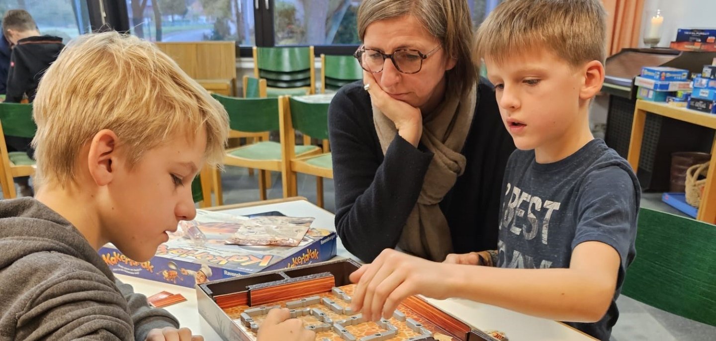 Eine Mutter sitzt mit ihren beiden Jungs an einem Tisch und spielt ein Gesellschaftsspiel.