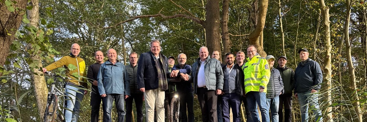 Eine Gruppe von etwa 15 Personen steht auf einem frisch angelegten Erdwall in einem Waldgebiet, vor ihnen ein grünes Rohr als Durchlass. Die Menschen posieren für ein Foto, einige tragen Outdoor- oder Arbeitskleidung.