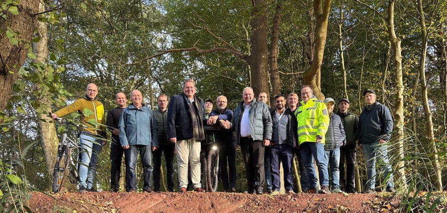 Eine Gruppe von etwa 15 Personen steht auf einem frisch angelegten Erdwall in einem Waldgebiet, vor ihnen ein grünes Rohr als Durchlass. Die Menschen posieren für ein Foto, einige tragen Outdoor- oder Arbeitskleidung.