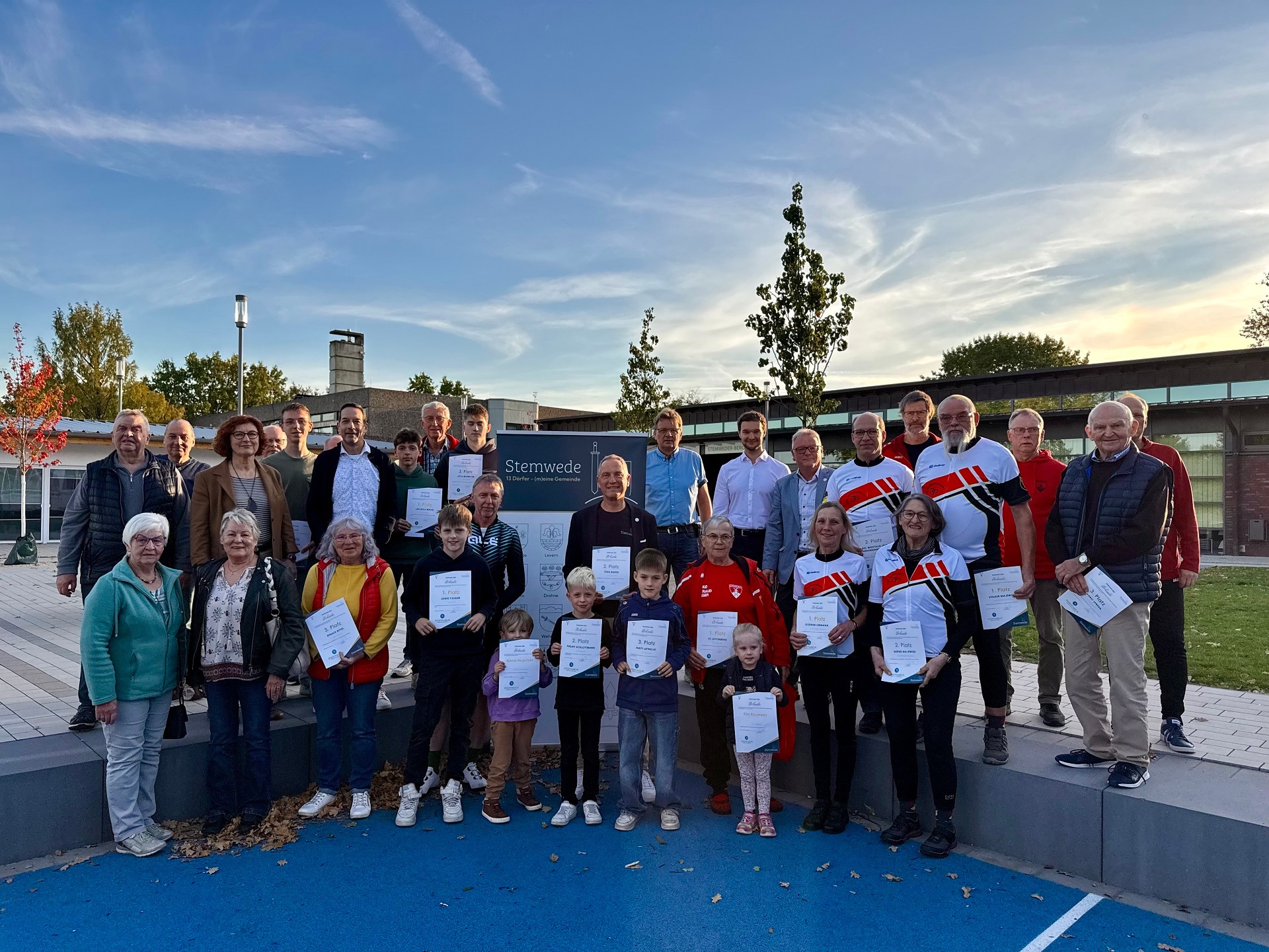 Zahlreiche Personen, zum Teil im sportlichen Outfit, die sich vor einem Gebäude für ein Gruppenfoto aufgestellt haben und Urkunden vor dem Körper halten.