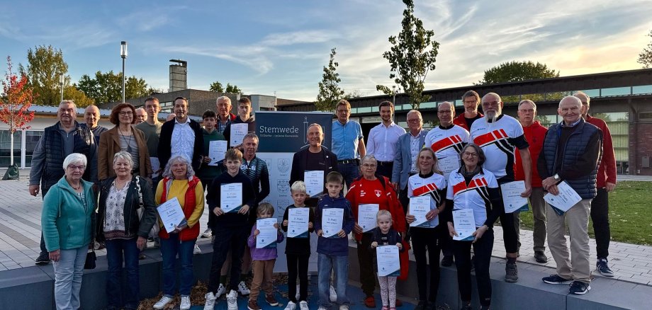 Zahlreiche Personen, zum Teil im sportlichen Outfit, die sich vor einem Gebäude für ein Gruppenfoto aufgestellt haben und Urkunden vor dem Körper halten.