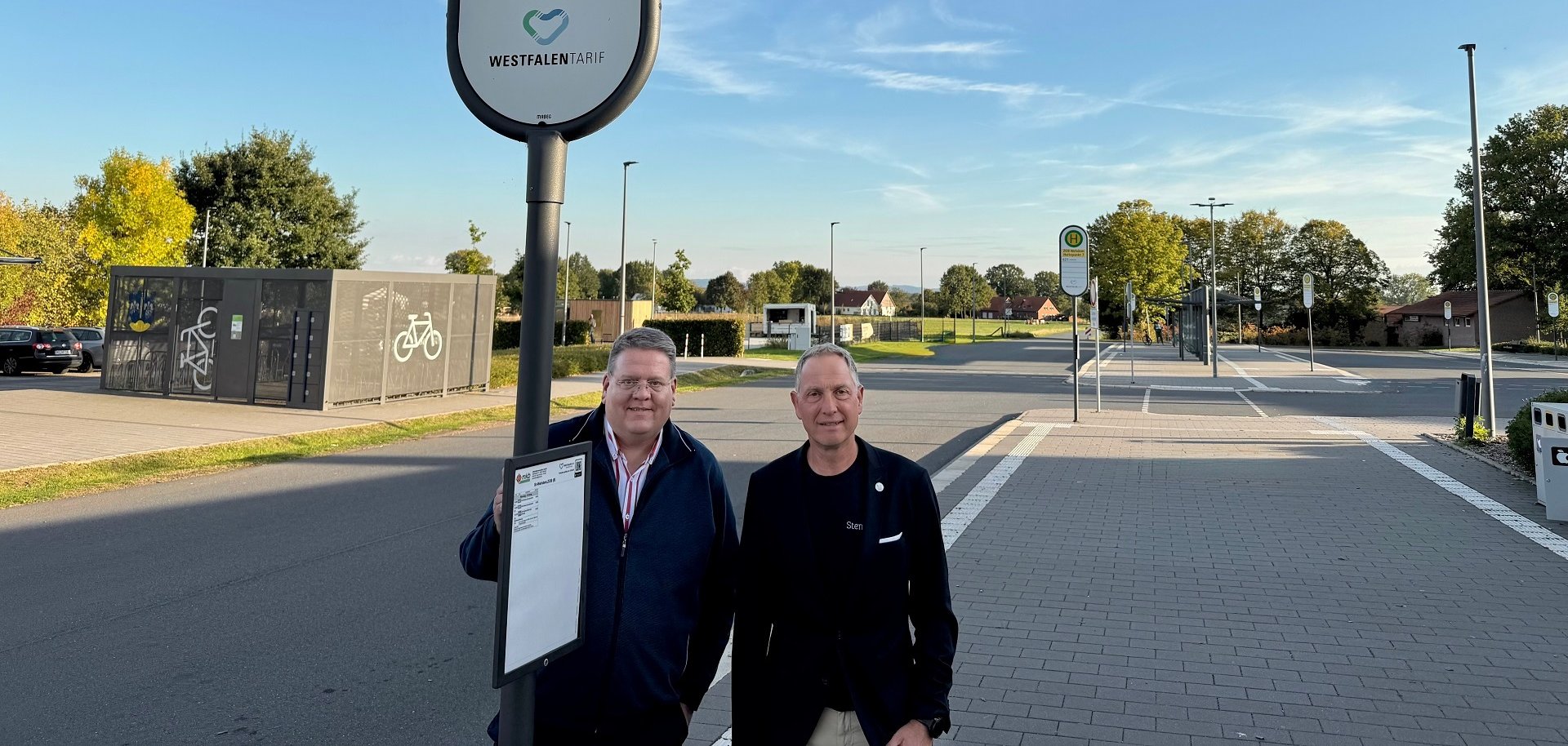 Zwei Männer an einem Bushaltestellenschild an einem Busbahnhof.