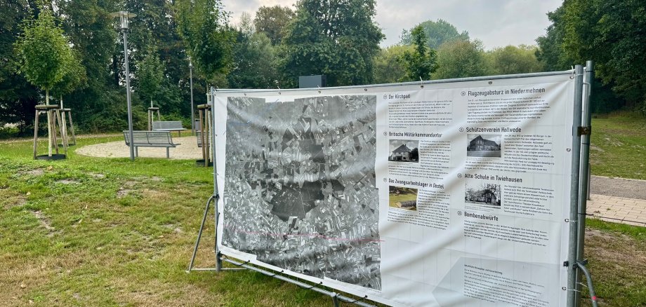 Großflächige Plakate an Bauzäunen in einem Park.
