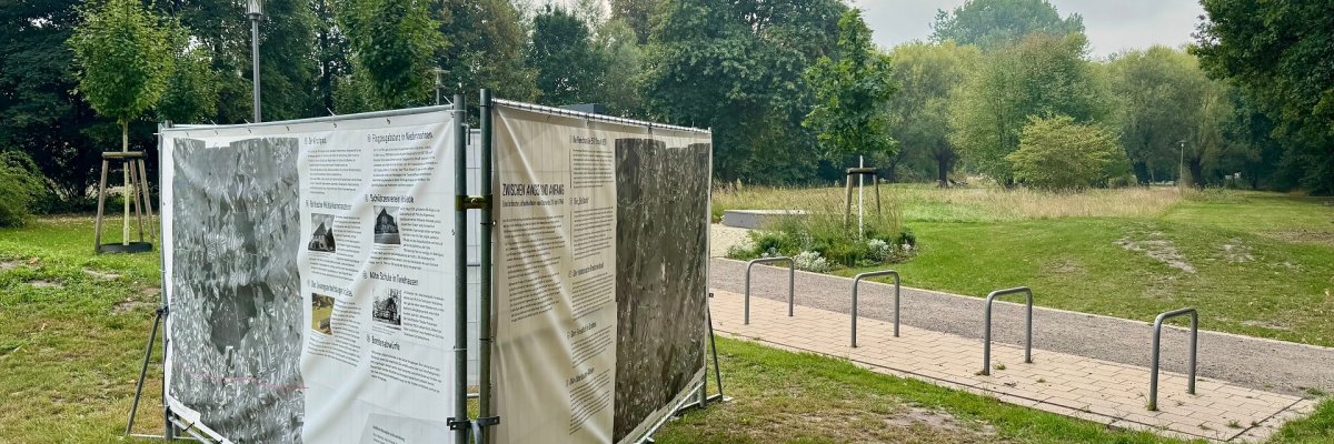 Ausstellung im Kurpark Großflächige Plakate an Bauzäunen in einem Park.