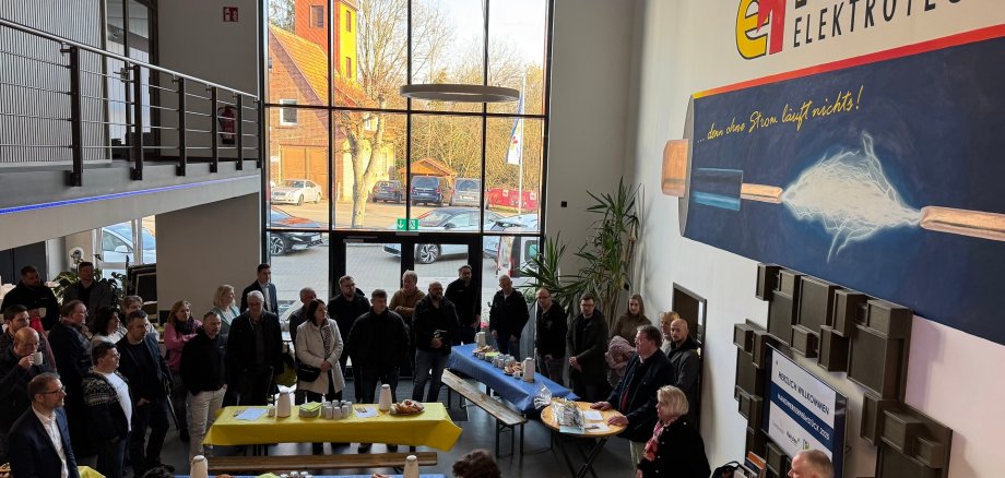 Handwerkerfrühstück 2025 Zahlreiche Personen im Foyer eines Unternehmens. Die Aufnahme wurde von der Galerie auf die Personen im Erdgeschoss gemacht. Die Personen scheinen stehen und sitzen im Foyer und scheinen einem Redner zuzuhören.