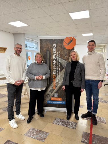 interkommunales Handwerkerfrühstück Zwei Männer und zwei Frauen in schickem Business-Outfit stehen vor einem Roll-Up der Kreishandwerkerschaft.