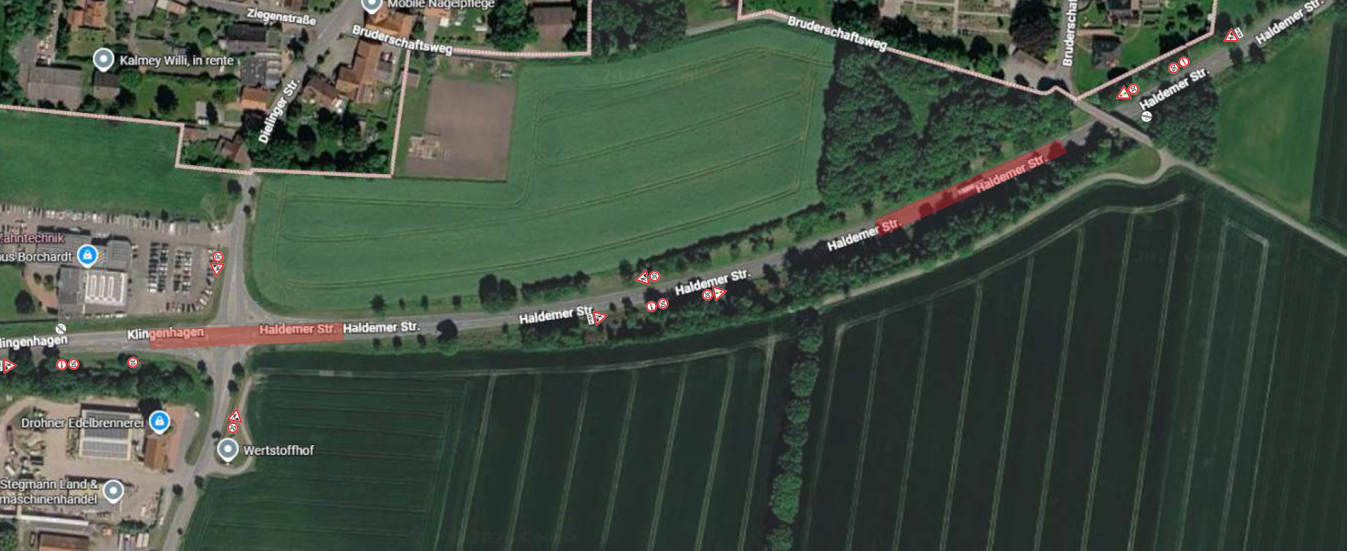Satellitenkarte eines Abschnitts der Haldemer Straße (L766) in Stemwede-Haldem. Rot markierte Bereiche kennzeichnen die Abschnitte, in denen Fahrbahnschäden saniert werden. Betroffen sind der Kreuzungsbereich Haldemer Straße/Dielinger Straße (K75) sowie ein weiterer Abschnitt vor der Überführung am Bruderschaftsweg. Mehrere Verkehrszeichen weisen entlang der Strecke auf die Baustelle, Fahrbahneinengungen und eine Geschwindigkeitsbegrenzung hin. Die Umgebung besteht überwiegend aus landwirtschaftlichen Flächen, Wald und vereinzelter Bebauung.