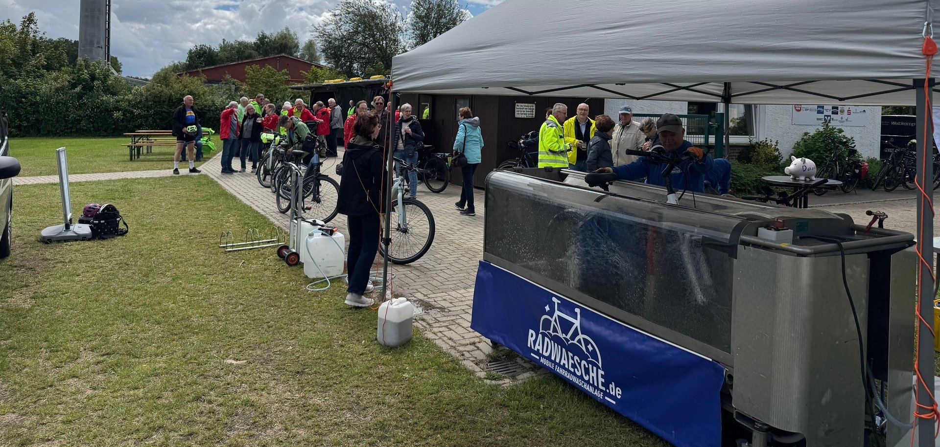 Mehrere Teilnehmerinnen und Teilnehmer des STADTRADELN-Abschlusstages warten mit ihren Fahrrädern vor einer mobilen Fahrradwaschanlage auf dem Sportplatz in Levern. Unter einem weißen Pavillon werden Fahrräder gereinigt, während sich weitere Gäste auf dem Veranstaltungsgelände austauschen. Die Waschanlage gehörte zu den beliebtesten Angeboten des Aktionstages.
