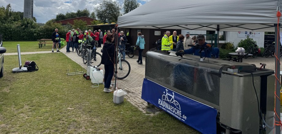 Mehrere Teilnehmerinnen und Teilnehmer des STADTRADELN-Abschlusstages warten mit ihren Fahrrädern vor einer mobilen Fahrradwaschanlage auf dem Sportplatz in Levern. Unter einem weißen Pavillon werden Fahrräder gereinigt, während sich weitere Gäste auf dem Veranstaltungsgelände austauschen. Die Waschanlage gehörte zu den beliebtesten Angeboten des Aktionstages.