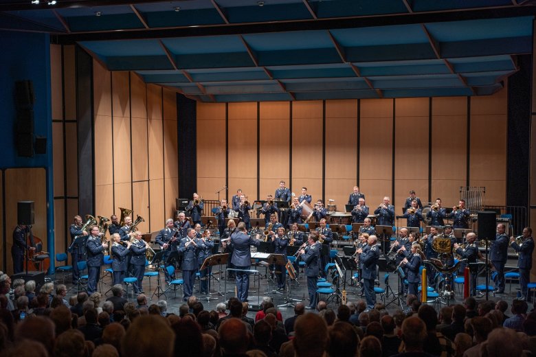 Luftwaffenmusikkorps Münster Ein Orchester auf einer Bühne. Im Vordergrund ist Publikum zu erkennen.