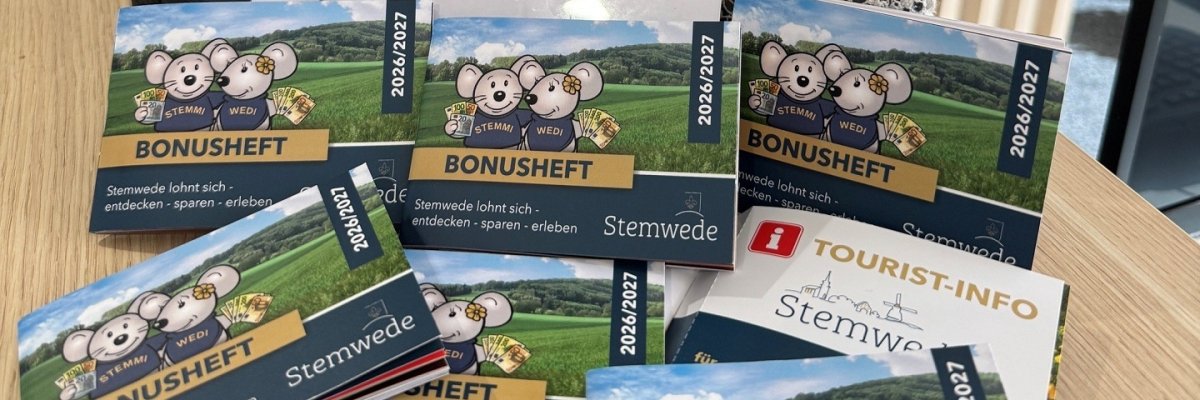 Bonusheft 2026 Mehrere Exemplare des Stemweder Bonushefts liegen auf einem Tisch in der Tourist-Info. Auf dem Titel sind die Maskottchen Stemmi und Wedi vor einer Landschaft zu sehen. Im Hintergrund stehen zwei Stoffmäuse mit Stemwede-Schals in einer dekorierten Holzkiste.