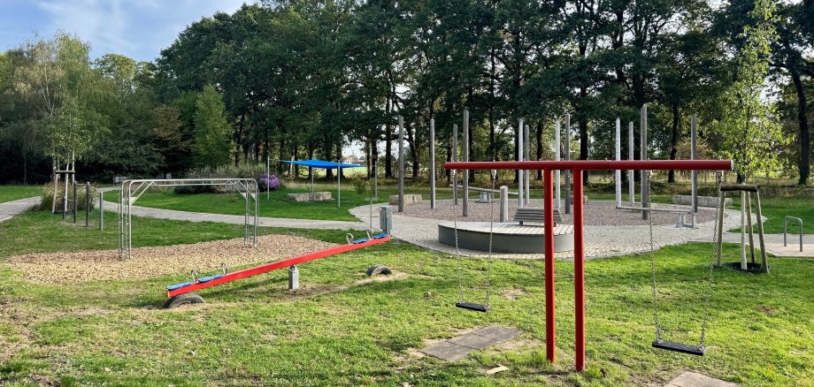 Spielplatz Kurpark Spielplatz im Grünen mit Doppelschaukel, Wippe, Klettergerüst und Sitzmöglichkeiten. Hohe Bäume rahmen die Anlage ein; im Hintergrund führt ein Weg durch den Park.
