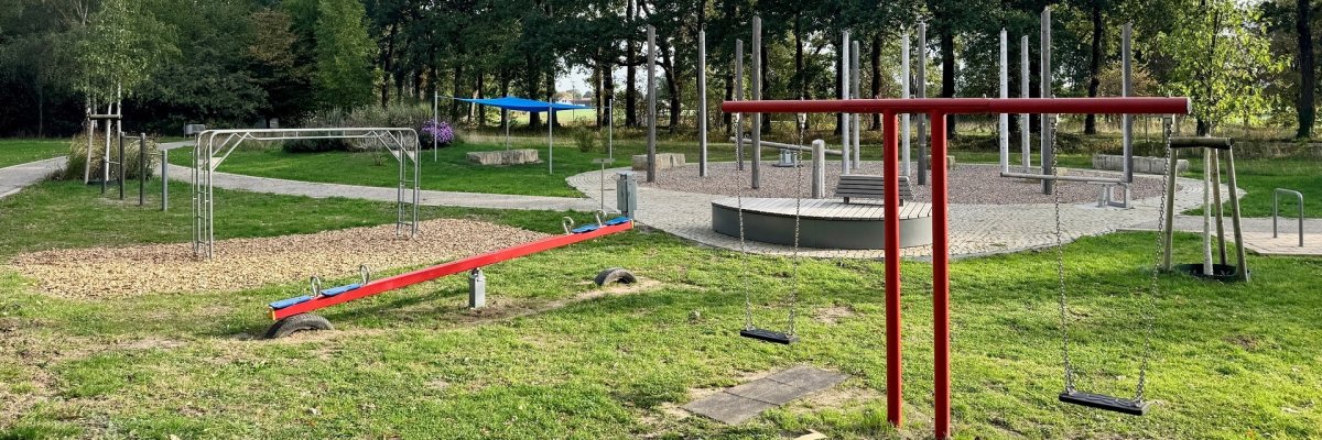 Spielplatz Kurpark Spielplatz im Grünen mit Doppelschaukel, Wippe, Klettergerüst und Sitzmöglichkeiten. Hohe Bäume rahmen die Anlage ein; im Hintergrund führt ein Weg durch den Park.
