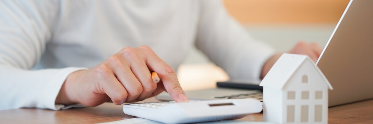Wohnbaufoerderung Mann sitzt am Schreibtisch und tippt etwas in einen Taschenrechner.
