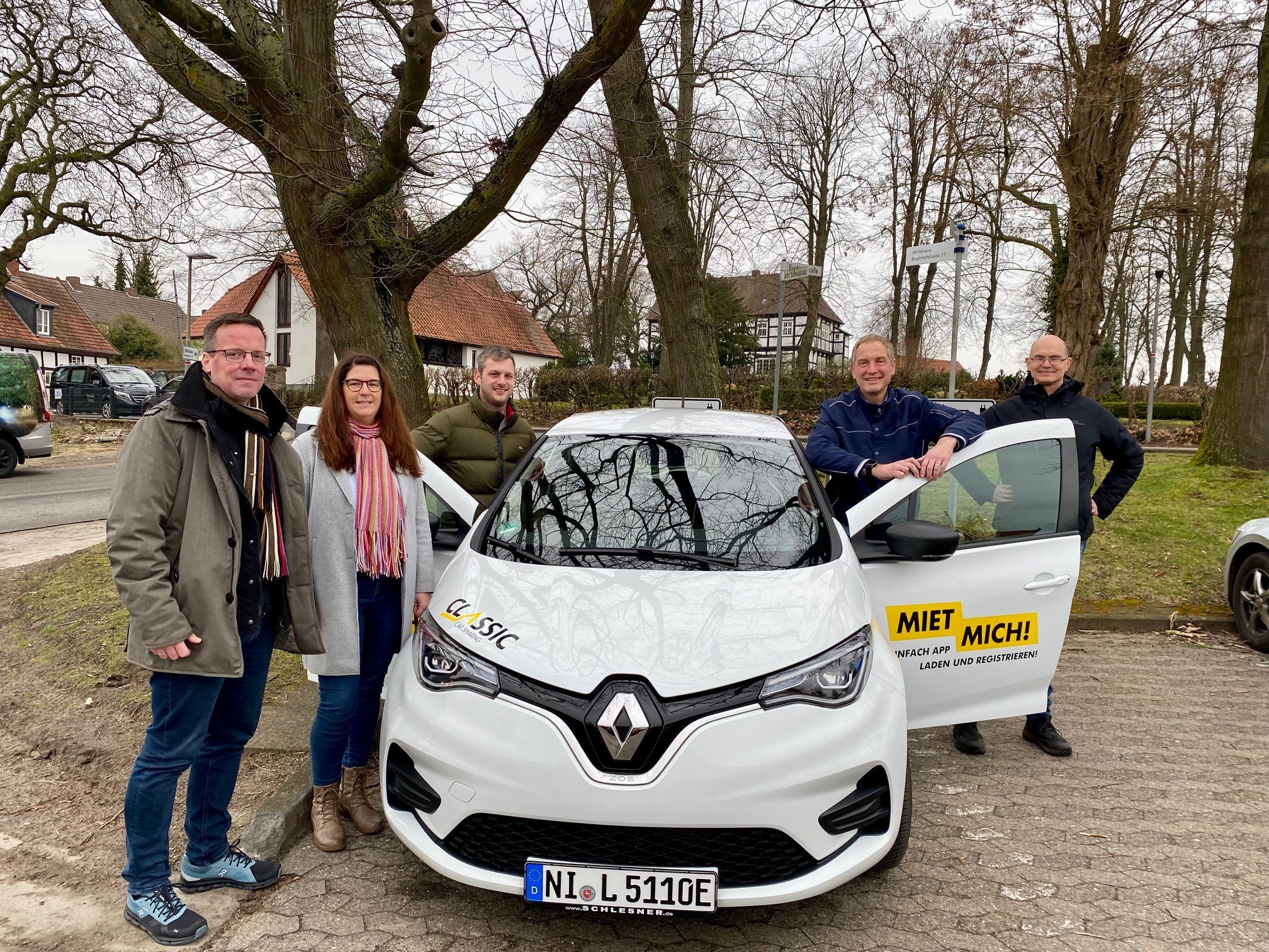 Gruppenfoto mit fünf Erwachsenen, die um ein weißes Auto stehen.
