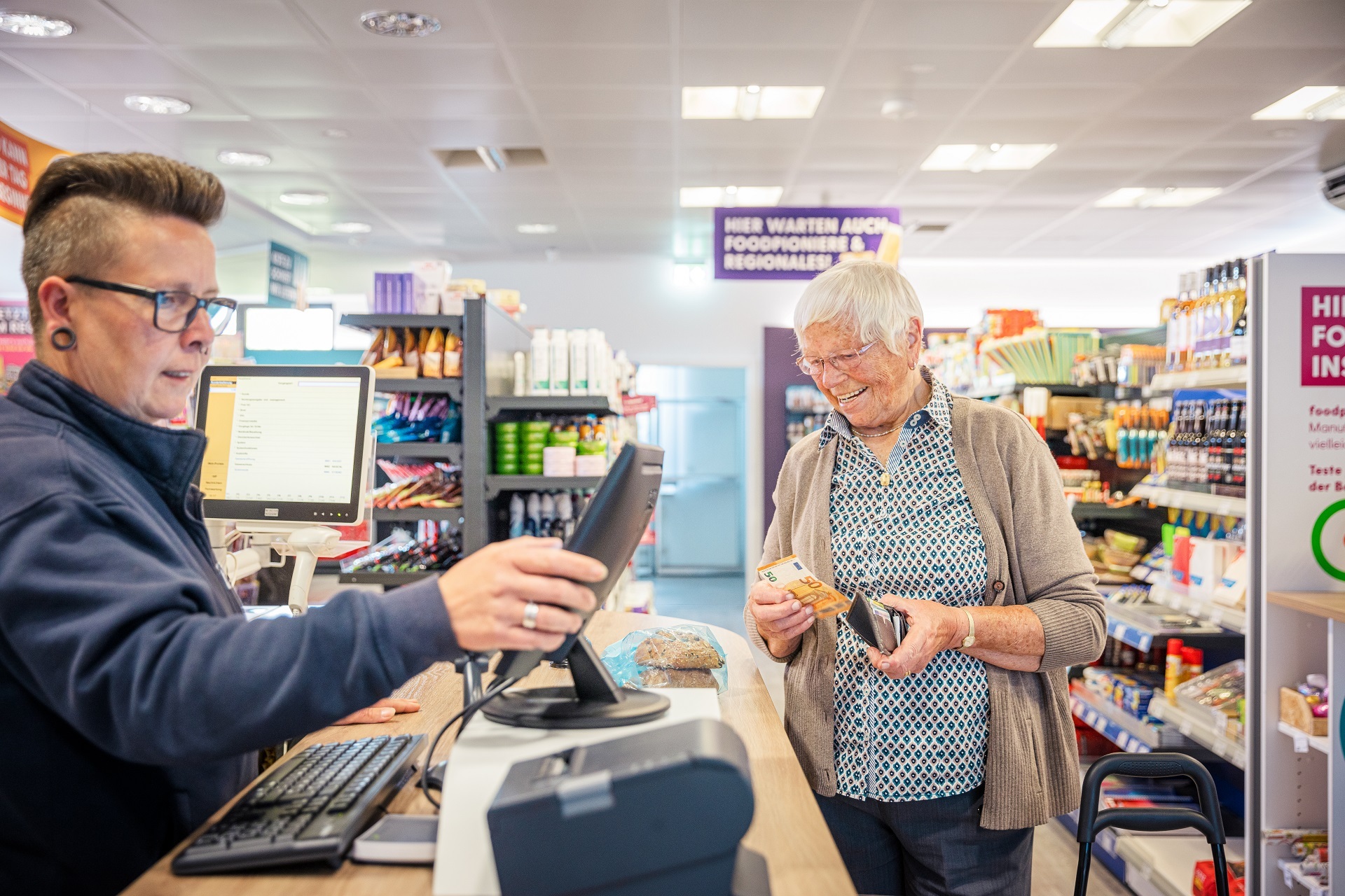 Eine Kassiererin in einem Supermarkt, die gerade eine ältere Kundin abrechnet. 