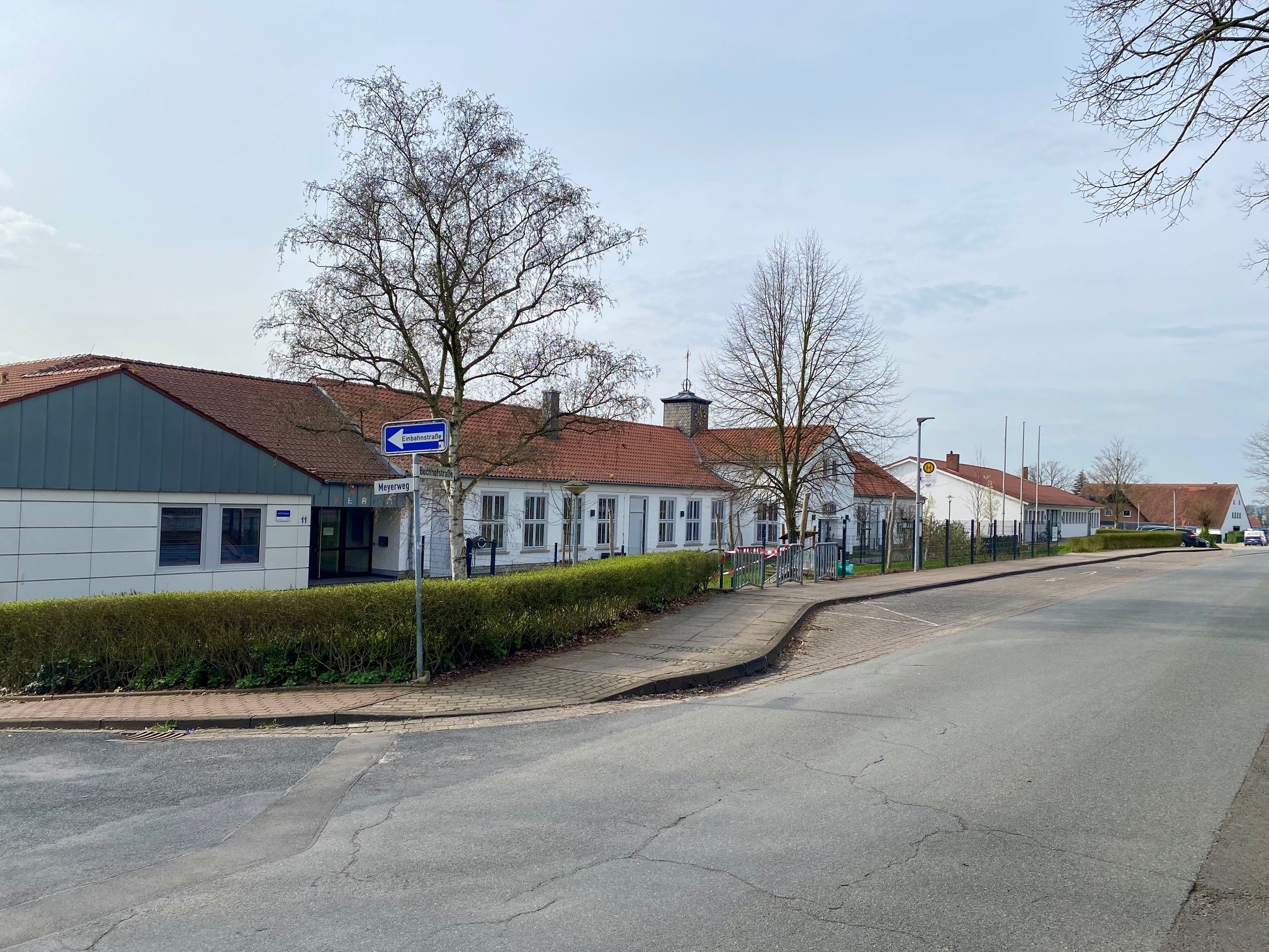 Ein weißes Schulgebäude mit einer davor verlaufenden Bushaltestelle an einer Straße. 