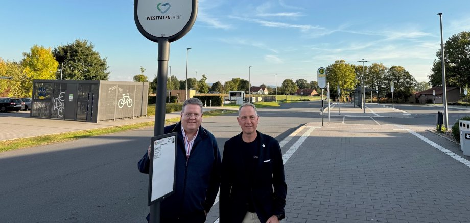 Zwei Männer an einem Bushaltestellenschild an einem Busbahnhof.