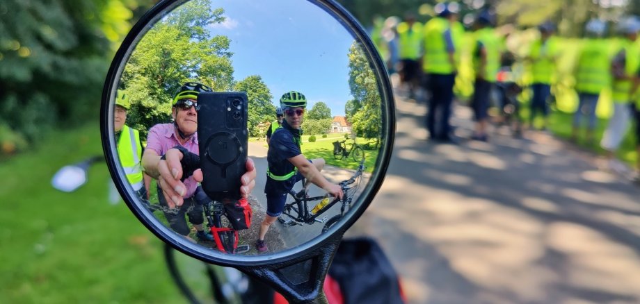 Ein Fahrradfahrer, der mit seinem Handy ein Foto aufnimmt, in dem er in den Fahrradspiegel fotografiert.