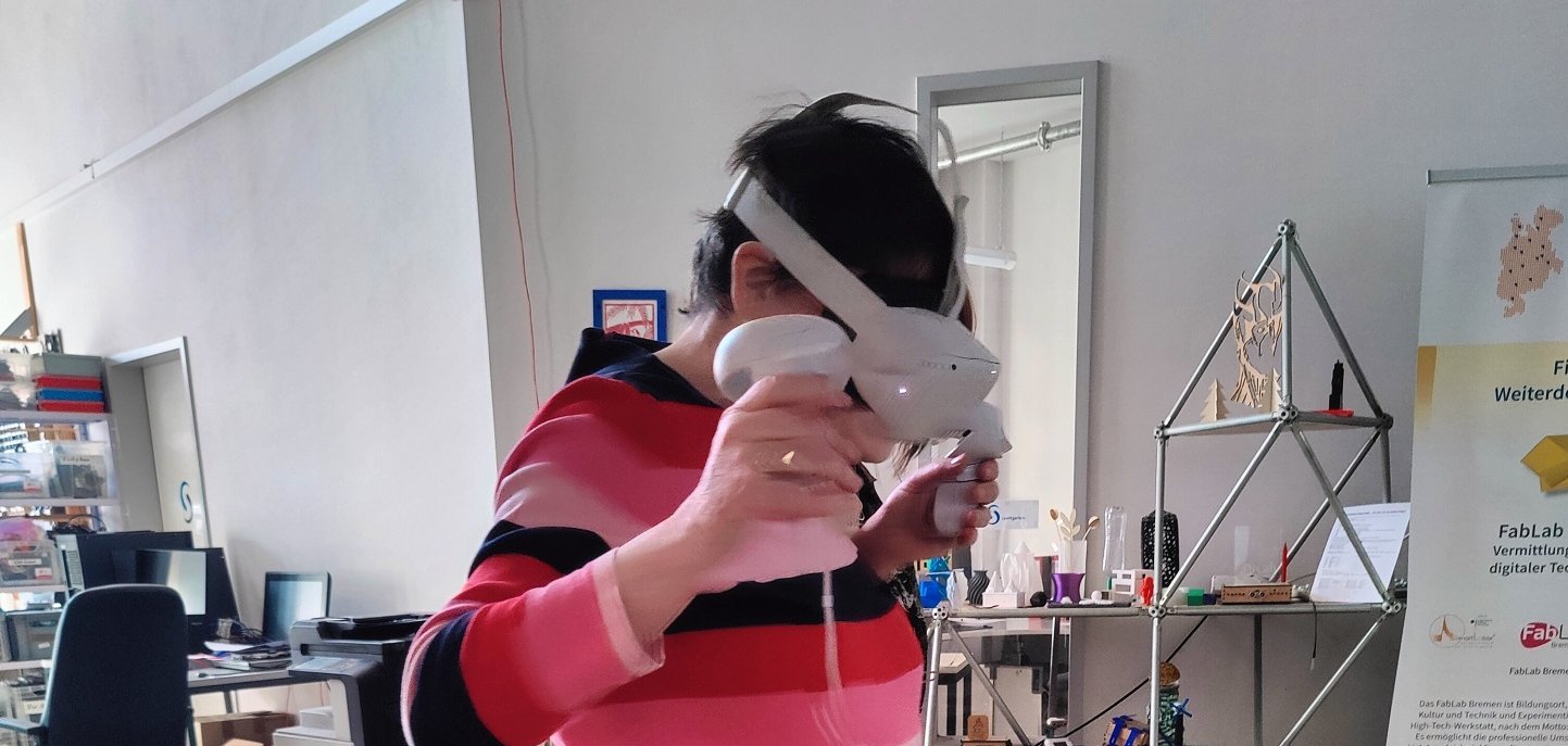 ZWAR-Bericht Person steht in einem offenen Kreativ- und Technikraum und nutzt eine Virtual-Reality-Brille mit zwei Controllern in den Händen. Im Hintergrund sind Arbeitsplätze, technische Geräte und Ausstellungsobjekte zu sehen.